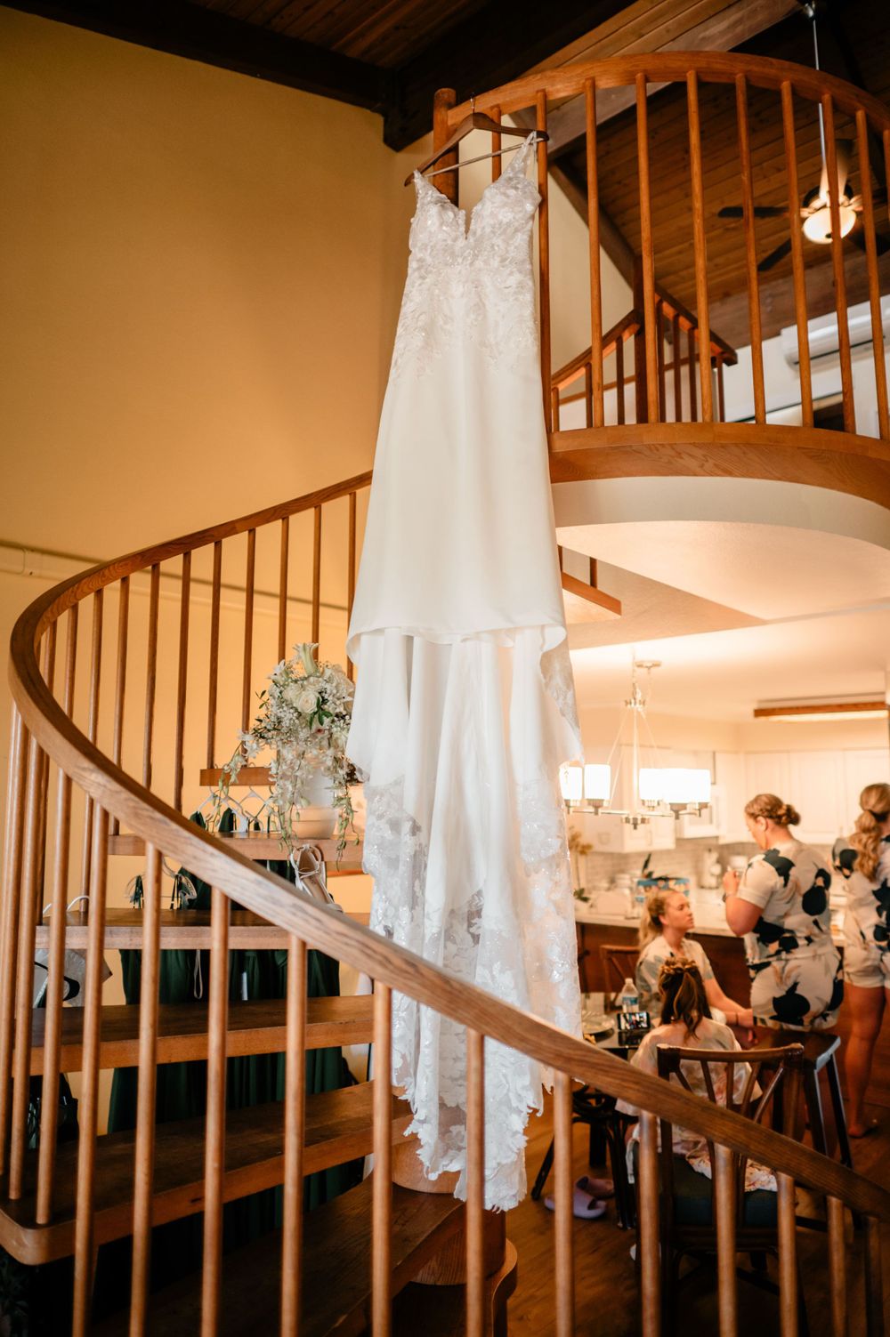 An elegant white lace wedding dress hangs on a curved wooden staircase railing.