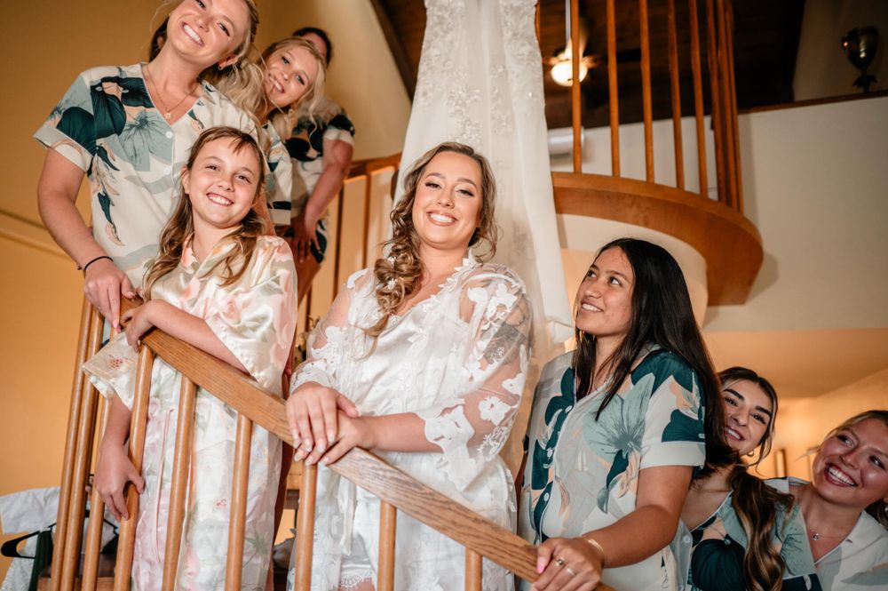 A joyful group poses on a spiral staircase during wedding preparations.