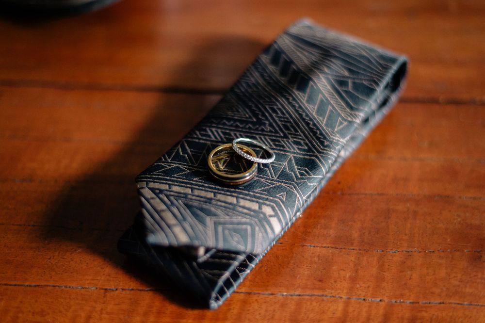 Wedding rings rest on a patterned navy blue tie on wooden surface.