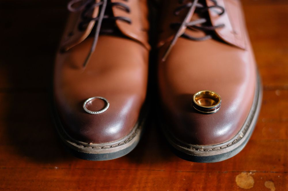 Wedding rings placed artistically on brown leather dress shoes.