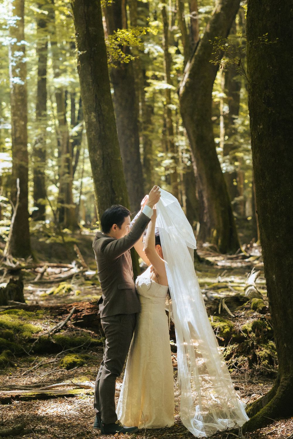A wedding couple and their photographer capture romantic moments in a sunlit forest setting.