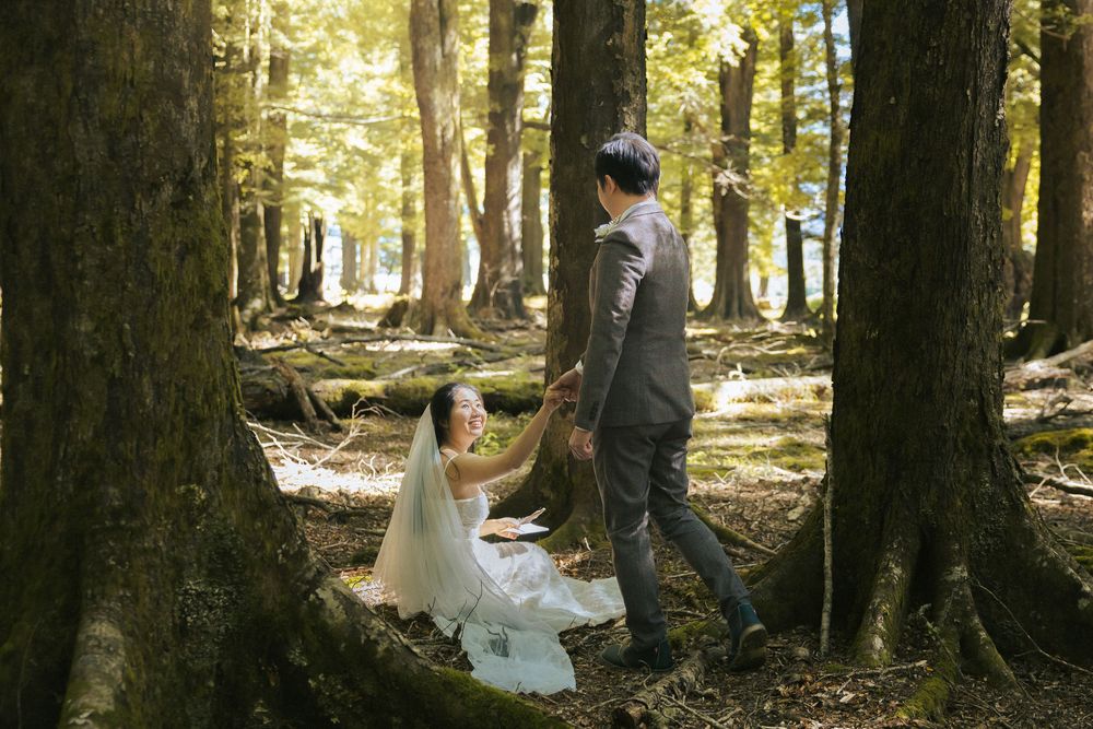 A couple shares an intimate moment in a sunlit forest setting during what appears to be a wedding photo session.