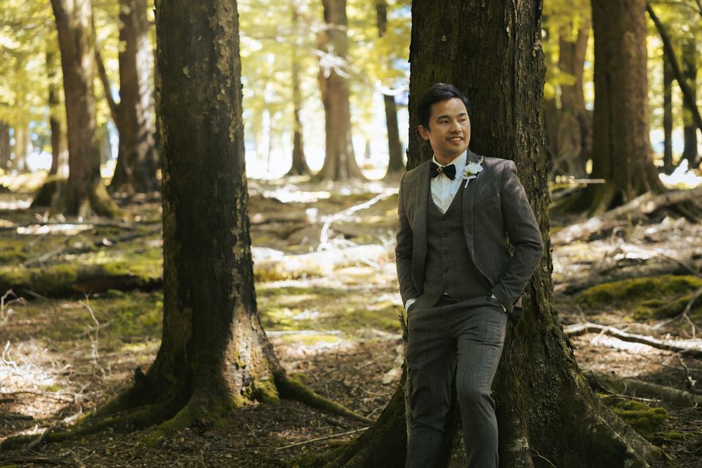 Wedding couple embraces in dappled sunlight filtering through a wooded forest.