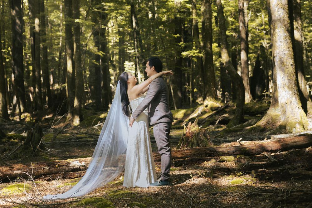 Newlyweds share an intimate moment among tall trees in a forest setting.