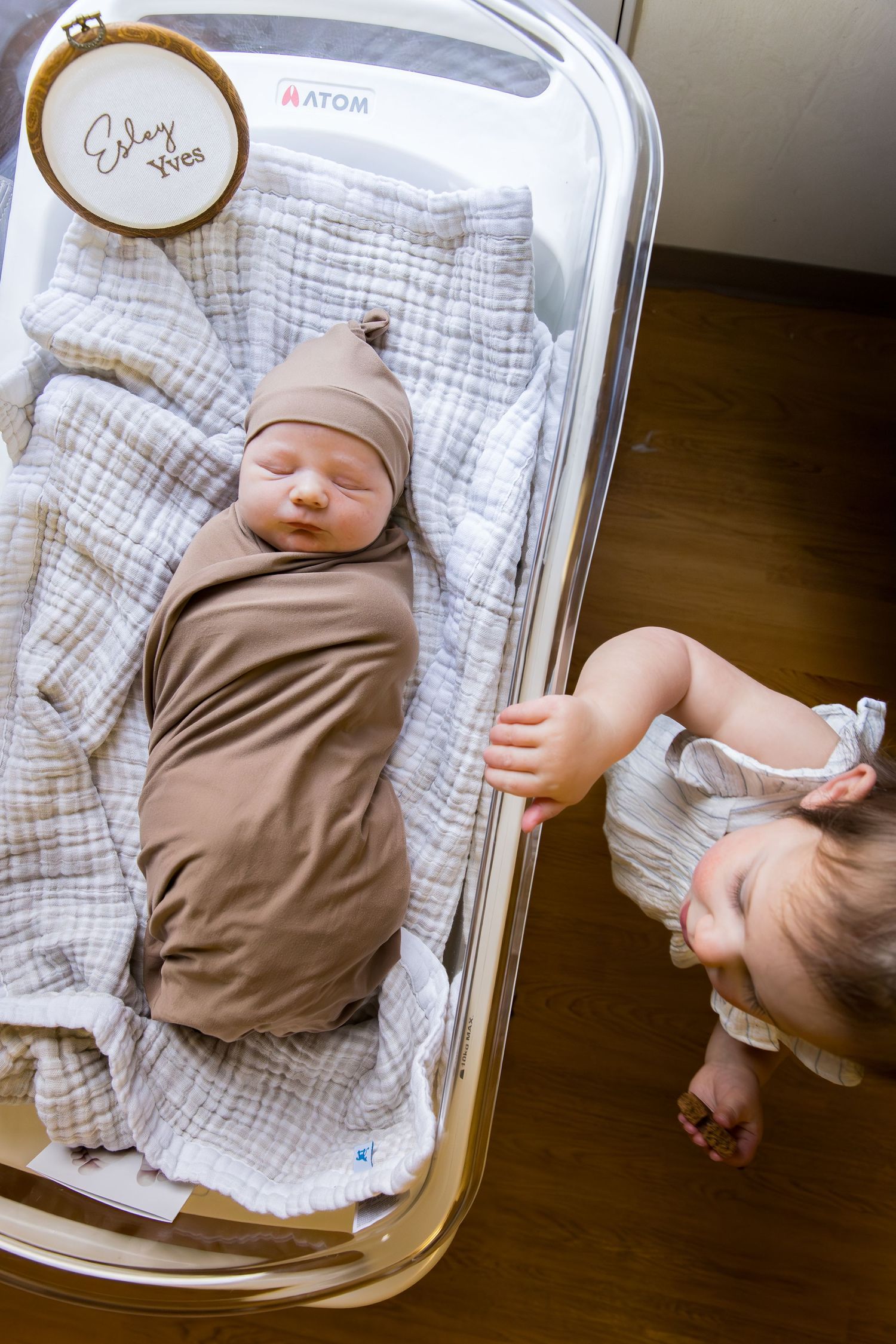 Overhead view of baby lying in white bassinet at hospital on checkered blanket. Fresh 48 photo session.