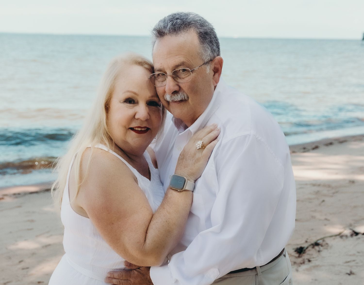 Couple in white clothing embracing on beach during sunset.