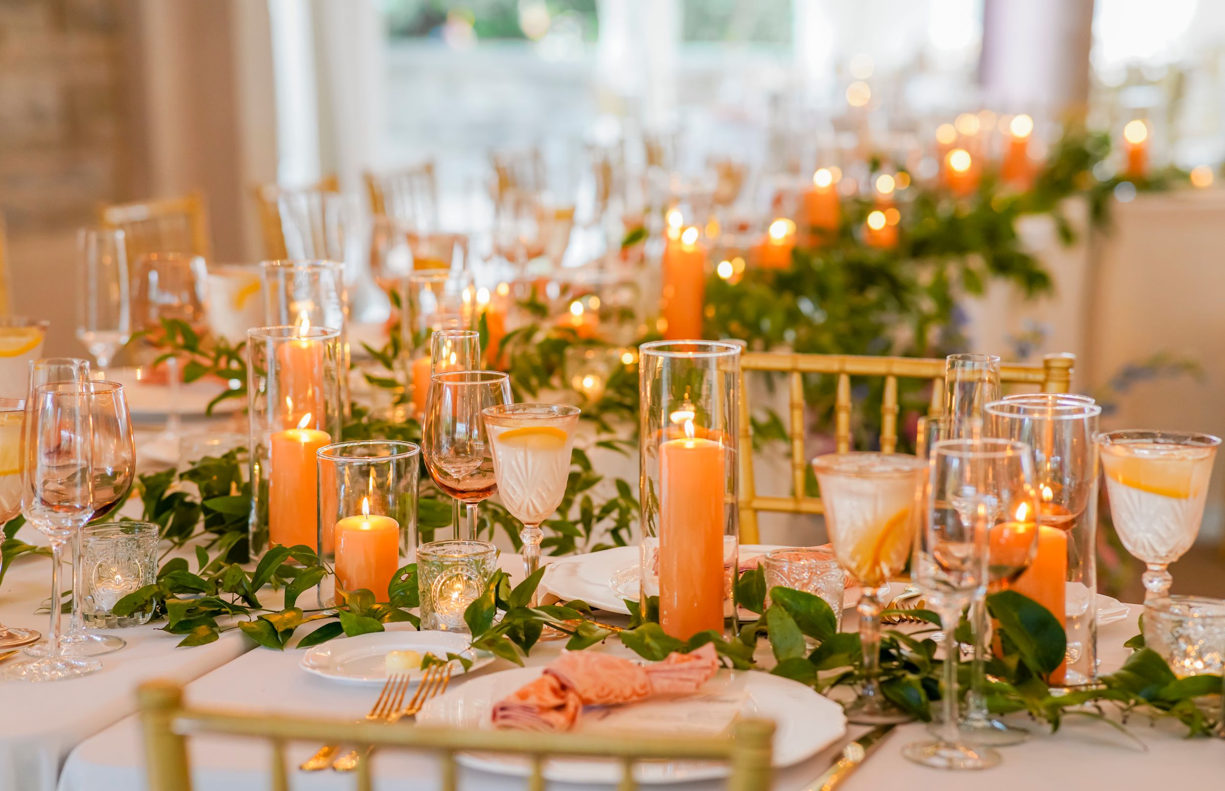 Elegant wedding reception table setting with orange candles and greenery garland centerpiece.