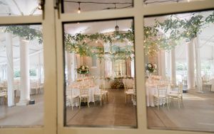 A panoramic view of an elegant white wedding reception tent with string lights and decorative chandeliers.