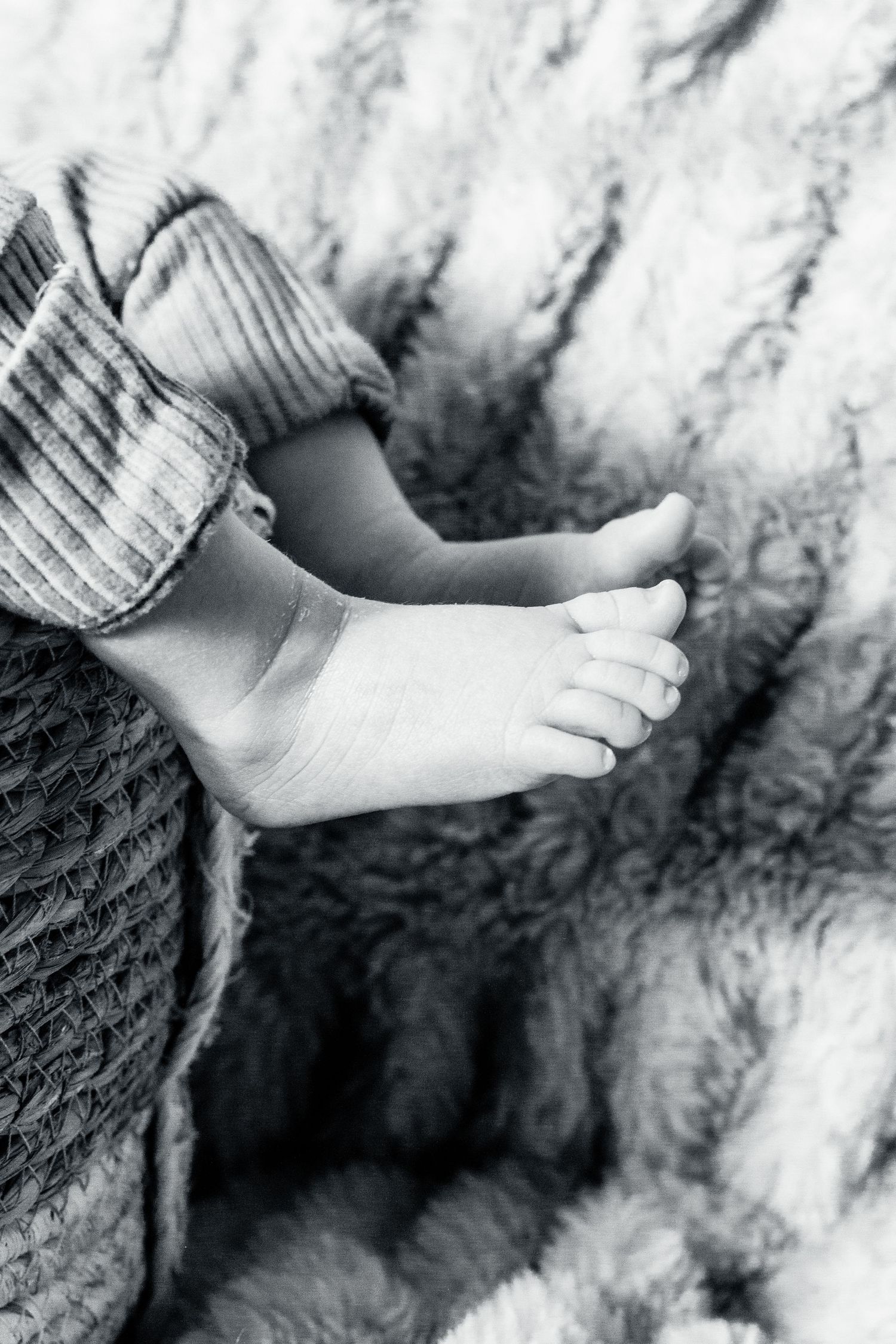 Black and white close-up of tiny baby feet resting on soft knitted blankets and textured fabric.