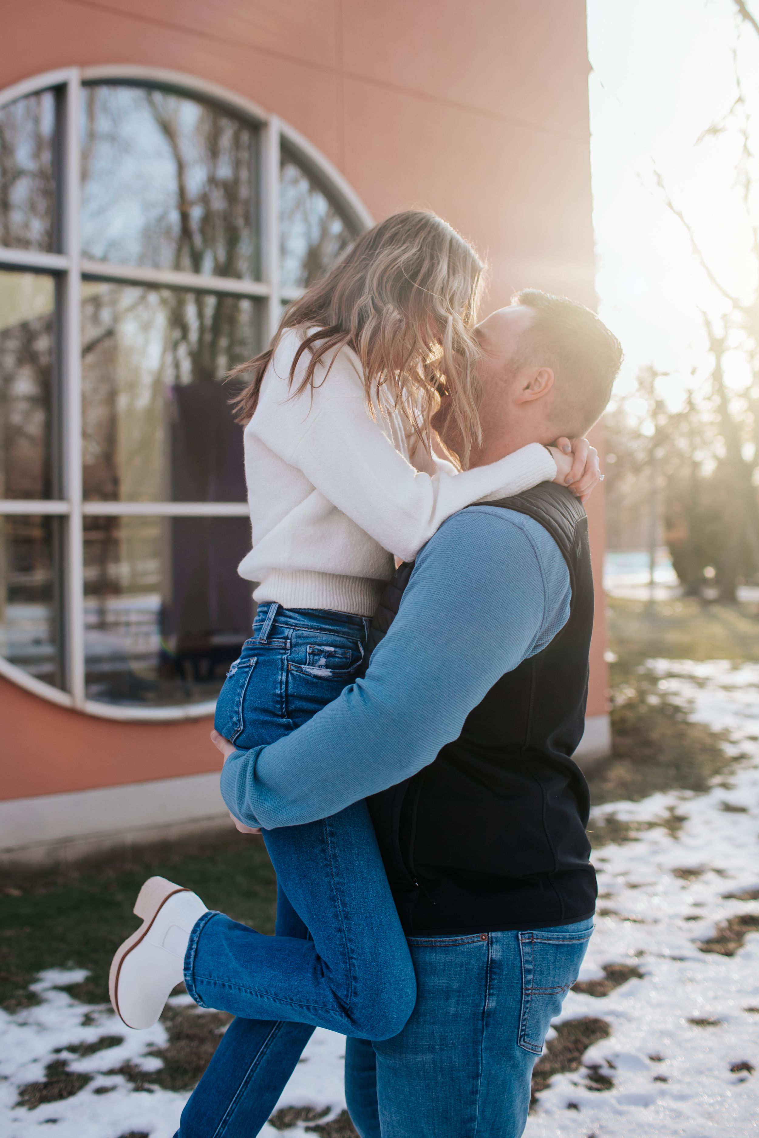 Romantic winter photoshoot with couple against building at sunset.