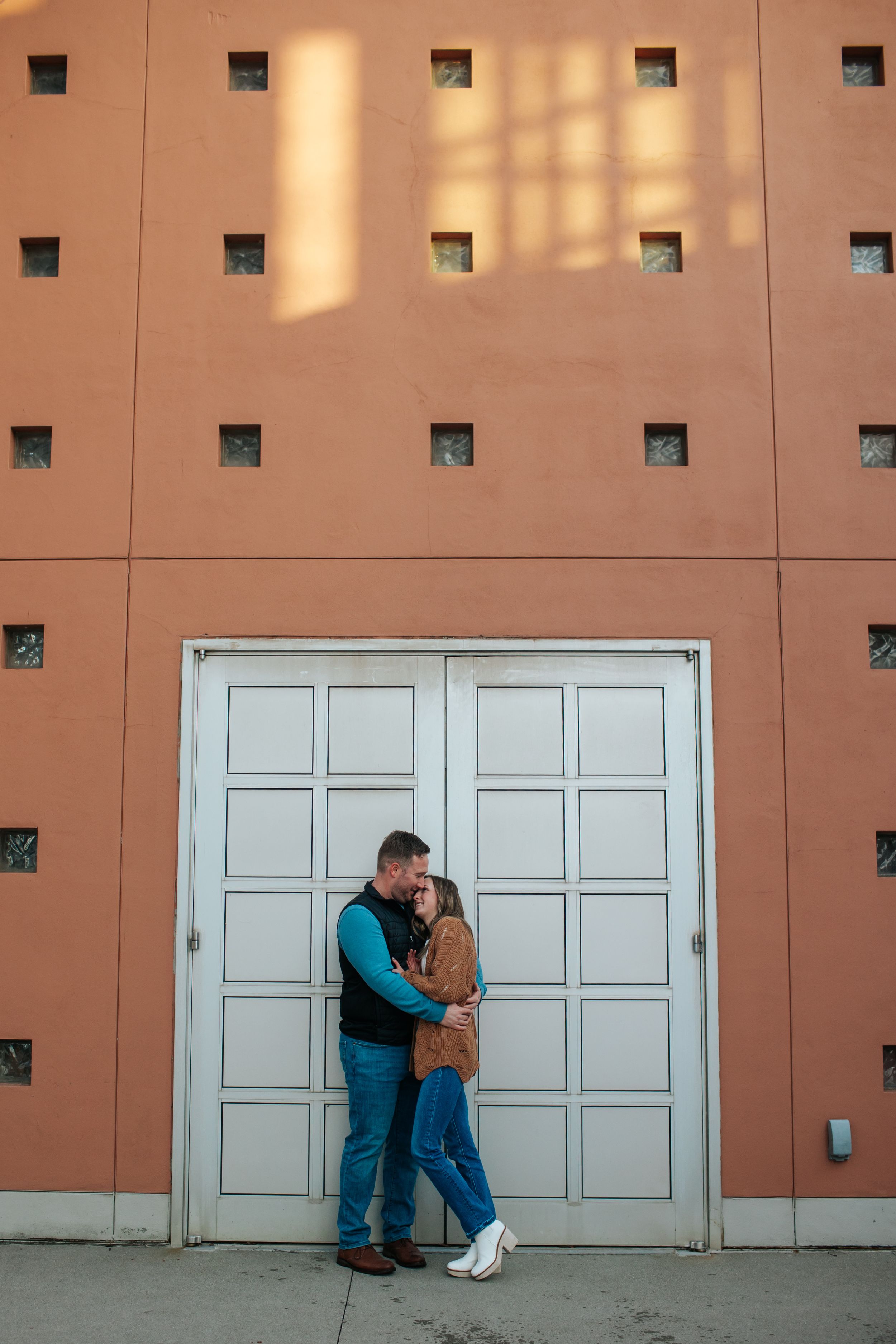 Couple poses against geometric wall with white doors and square patterns.