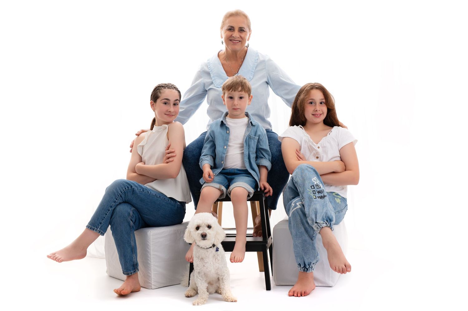 A family in coordinated blue and neutral tones poses against a dark backdrop in a professional portrait session.