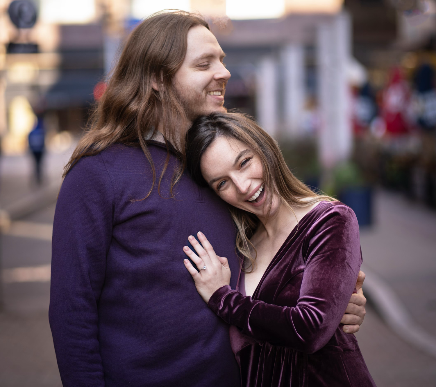A couple embraces and laughs together on a city street during an engagement session