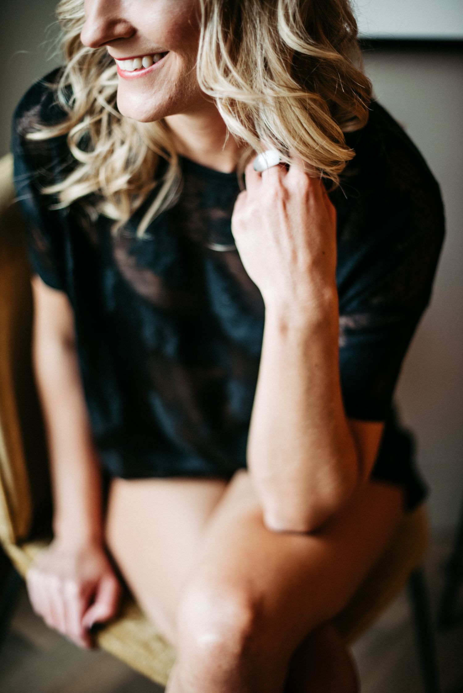 Eine blonde Frau mit nackten Beinen sitzt auf einem Stuhl und lächelt.