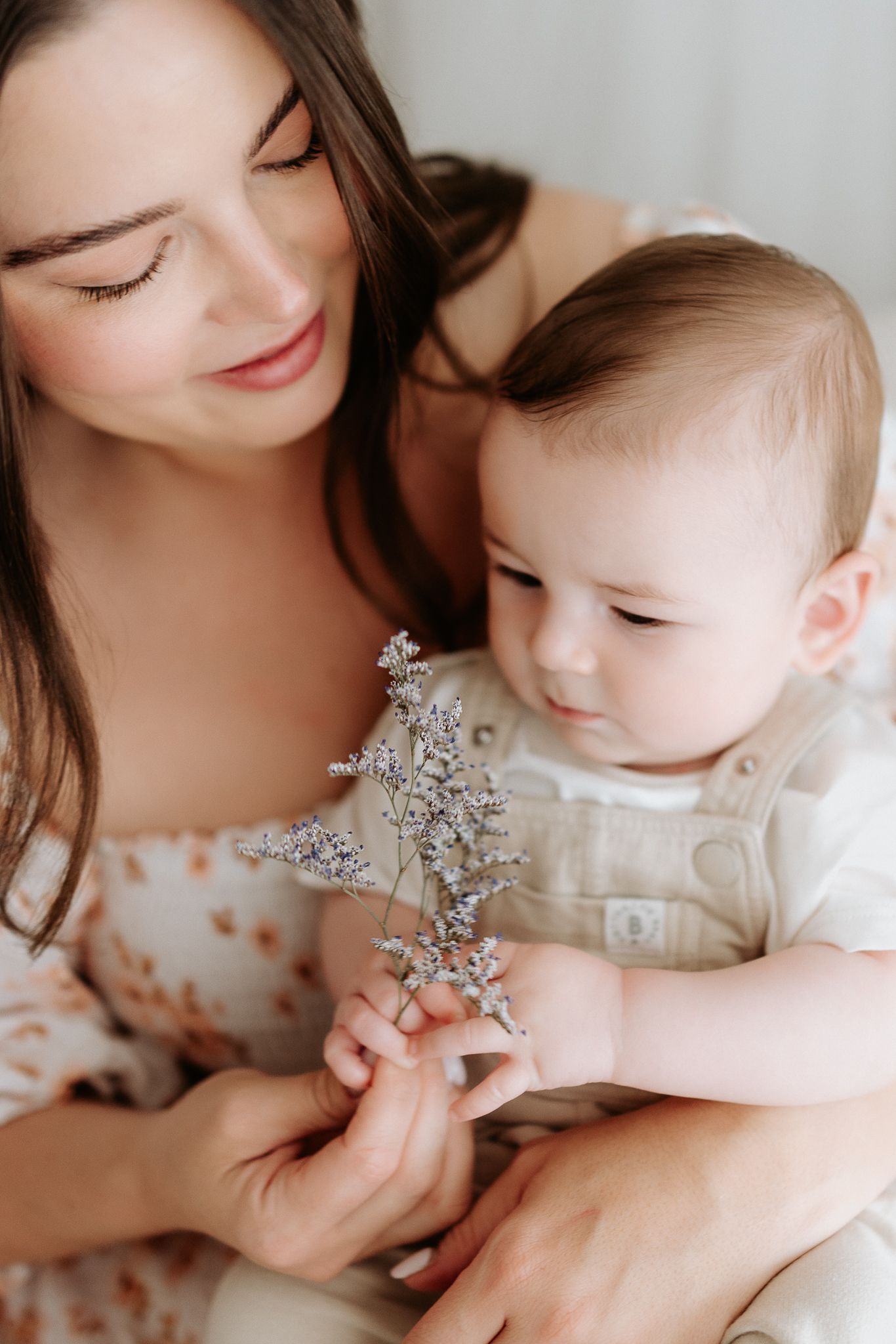 A baby in white clothing examines a small silver charm or pendant while lying down.