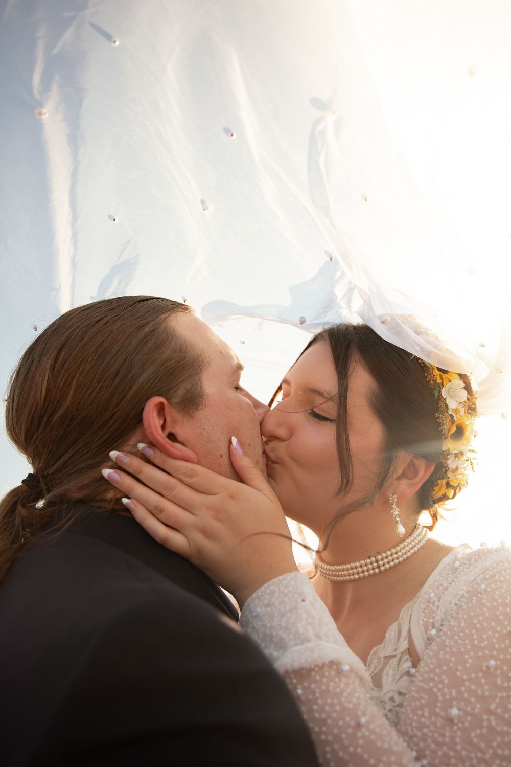 A tender romantic moment captured through a delicate white veil during a beach wedding ceremony.