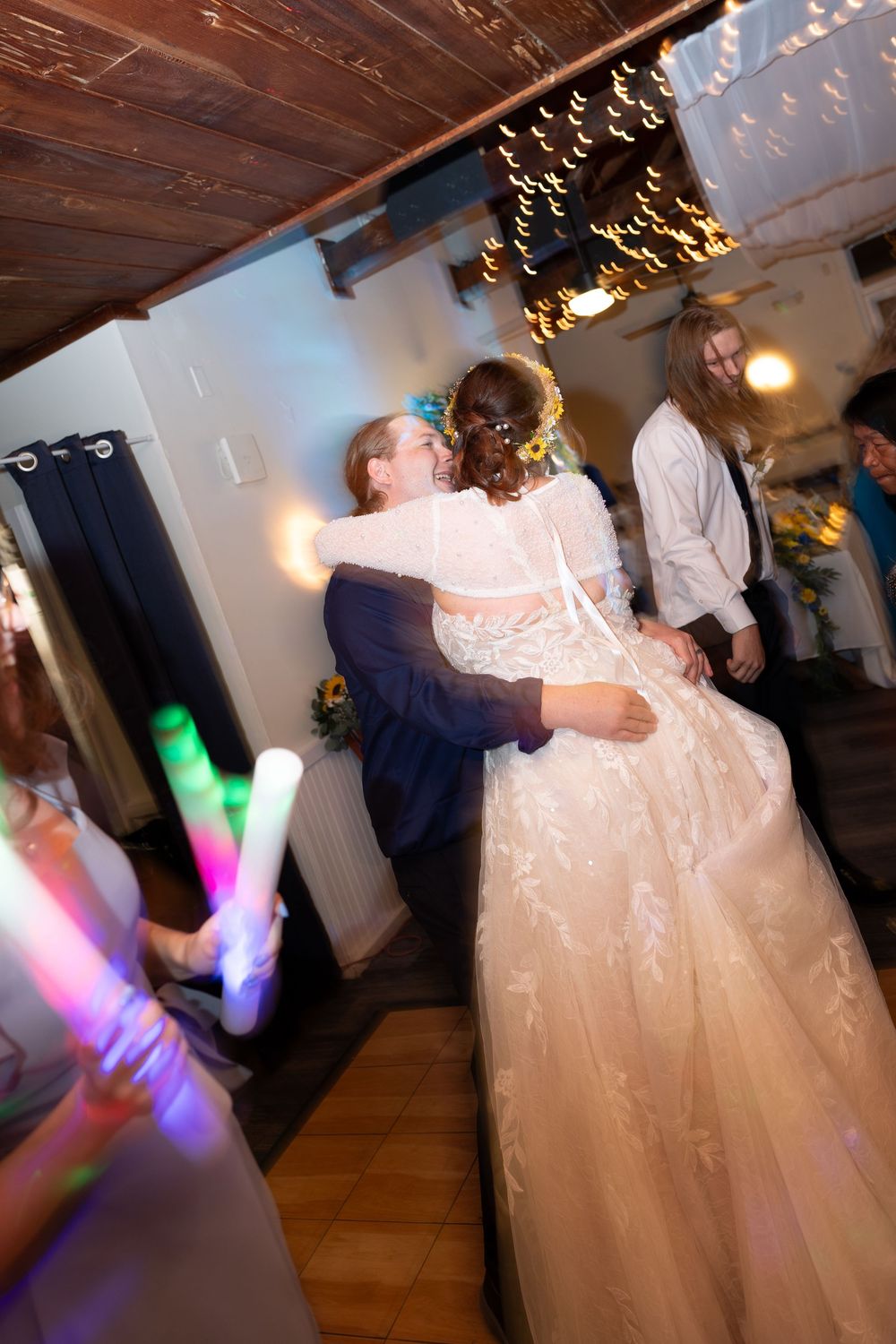 A couple shares their first dance at a wedding reception under twinkling lights and colorful disco beams.