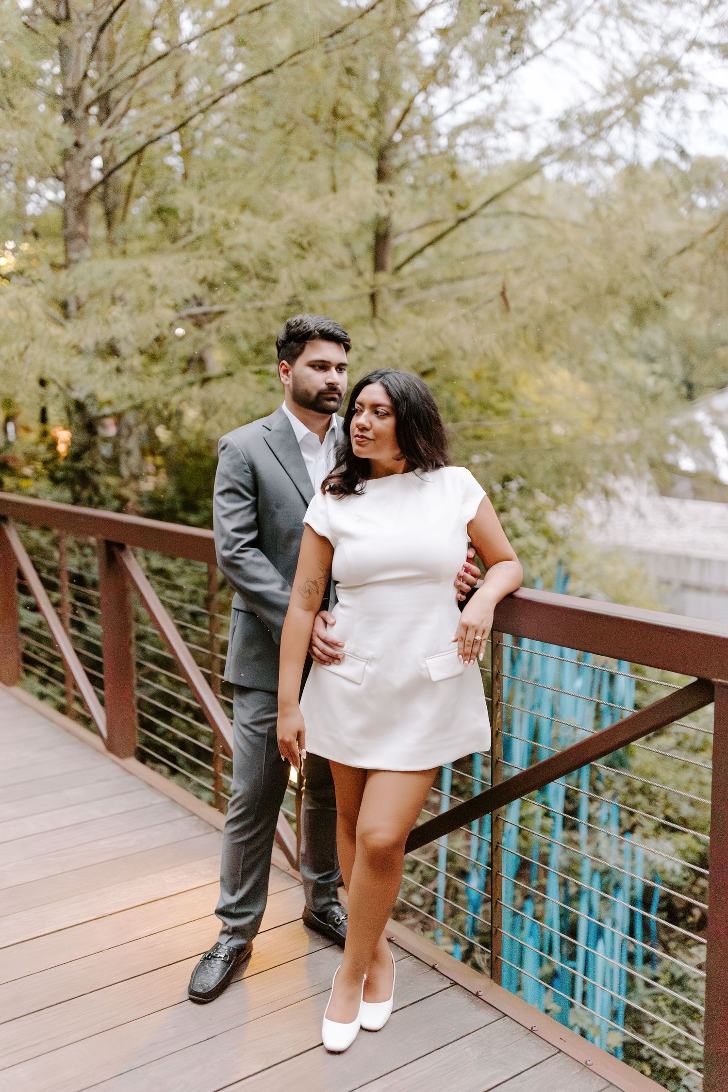 A couple poses together on a wooden bridge deck surrounded by autumn trees at Crystal Bridges Museum of American Art.