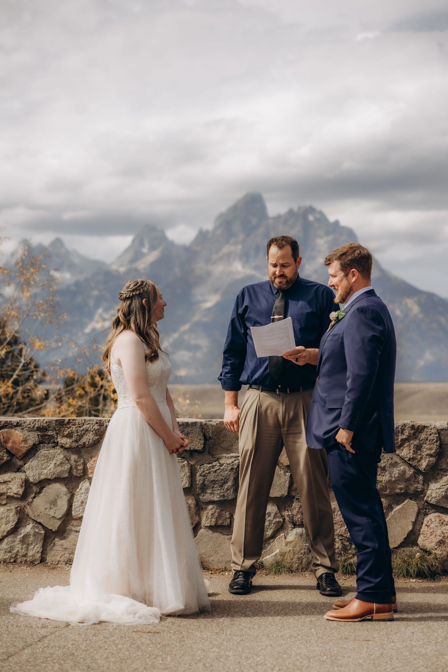 Intimate wedding ceremony takes place against dramatic mountain backdrop with stone wall in foreground.