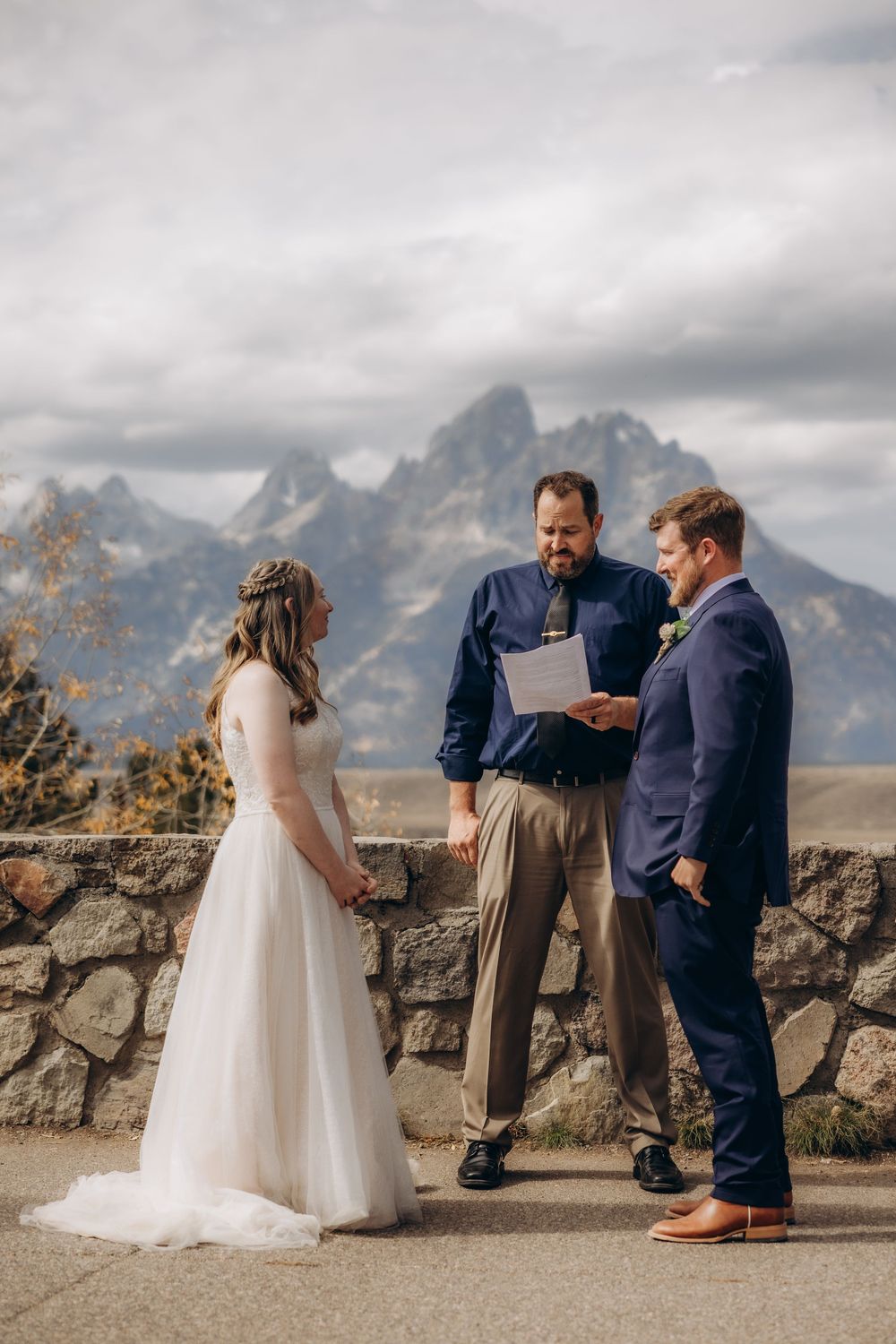 Intimate wedding ceremony takes place against dramatic mountain backdrop with stone wall in foreground.