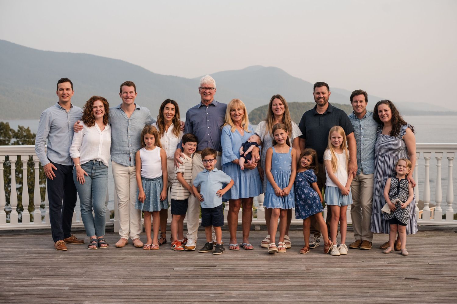 Family group wearing coordinated blue and white outfits poses together on beach boardwalk at sunset.