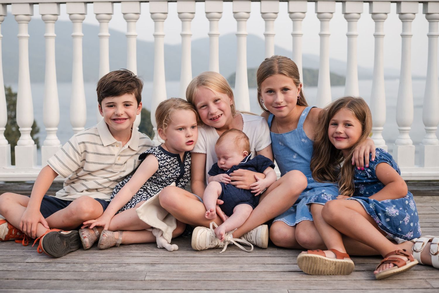 A group of children sit together on white porch steps during a casual outdoor photo session.