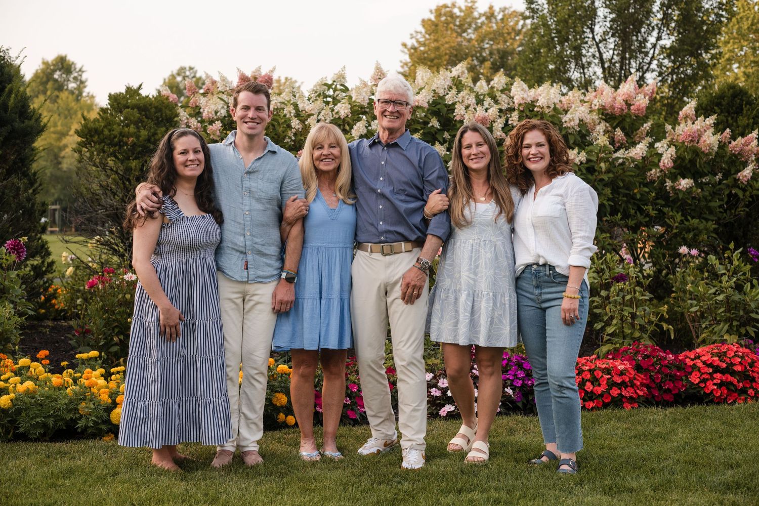 A group wearing coordinated blue and white outfits poses together in a blooming garden setting.