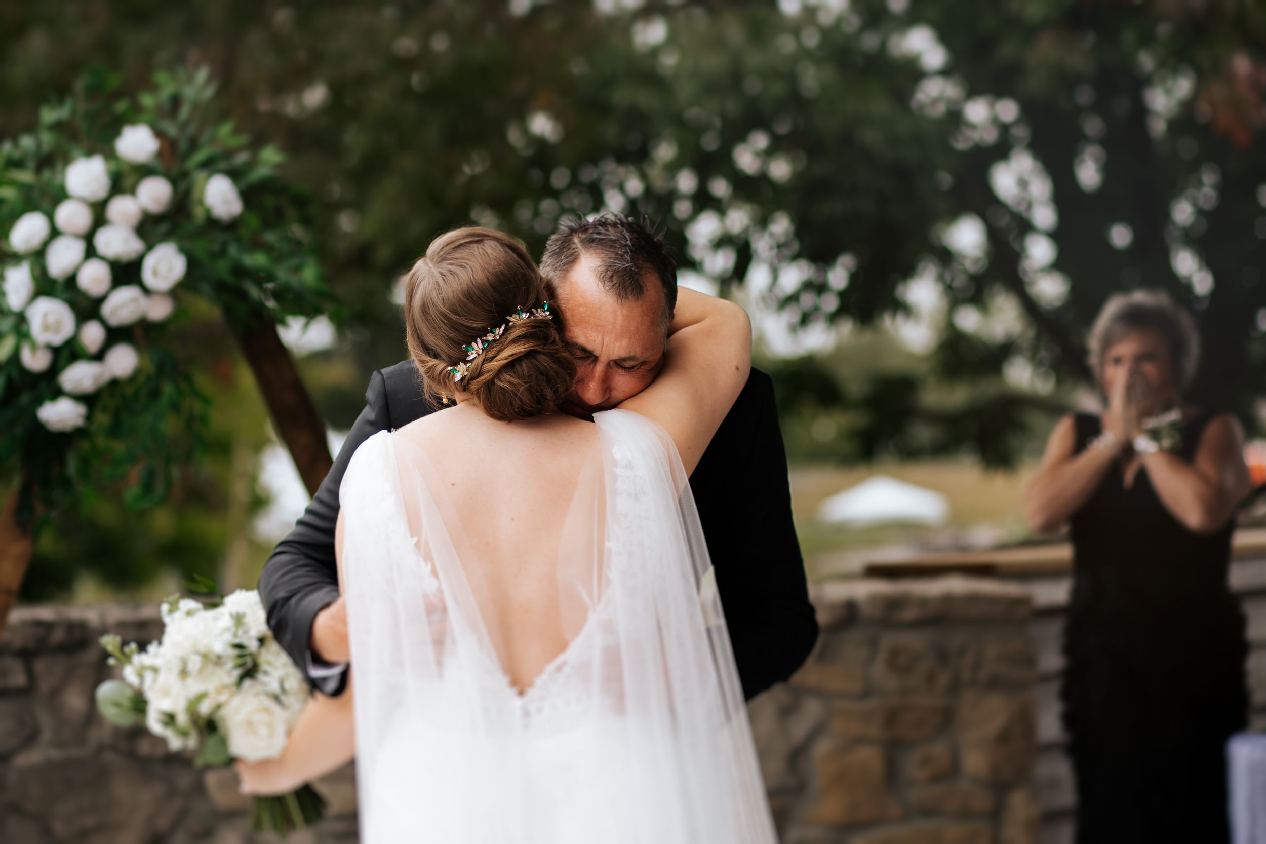 A father embraces his daughter on her wedding celebration in a romantic garden setting with string lights overhead. Conner Prairie, Fishers