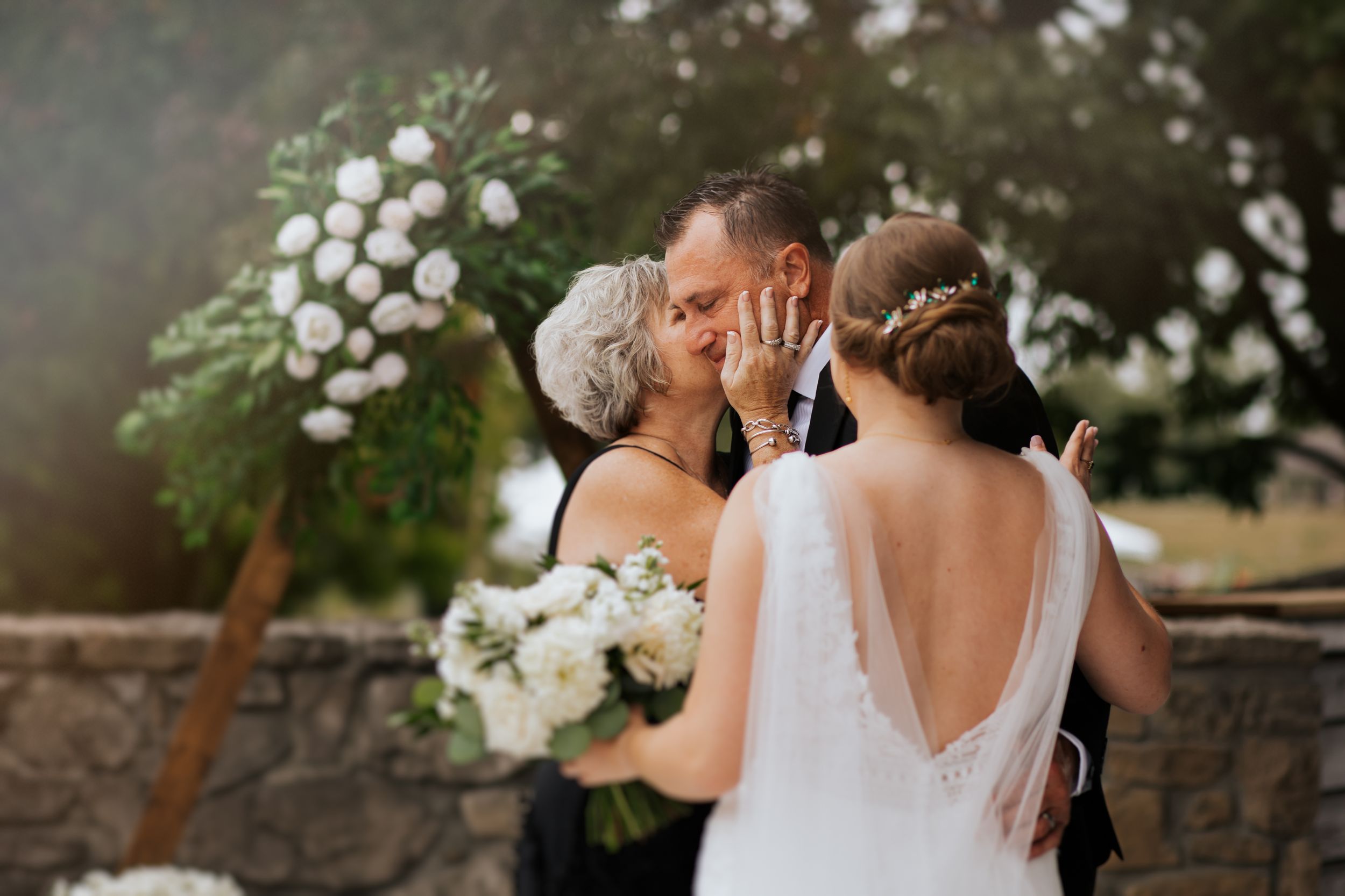 A romantic outdoor wedding scene with white floral arrangements and natural stone decor at sunset.