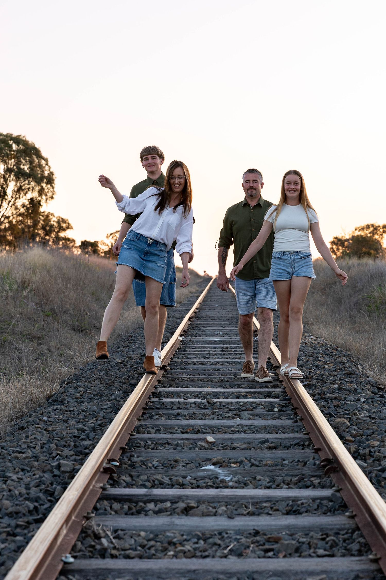 Family walking and balancing on railway lines at sunset in professional family photo shoot