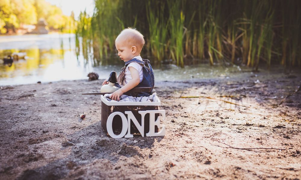 A baby explores the beach at golden hour while crawling on sandy ground near tall grass.