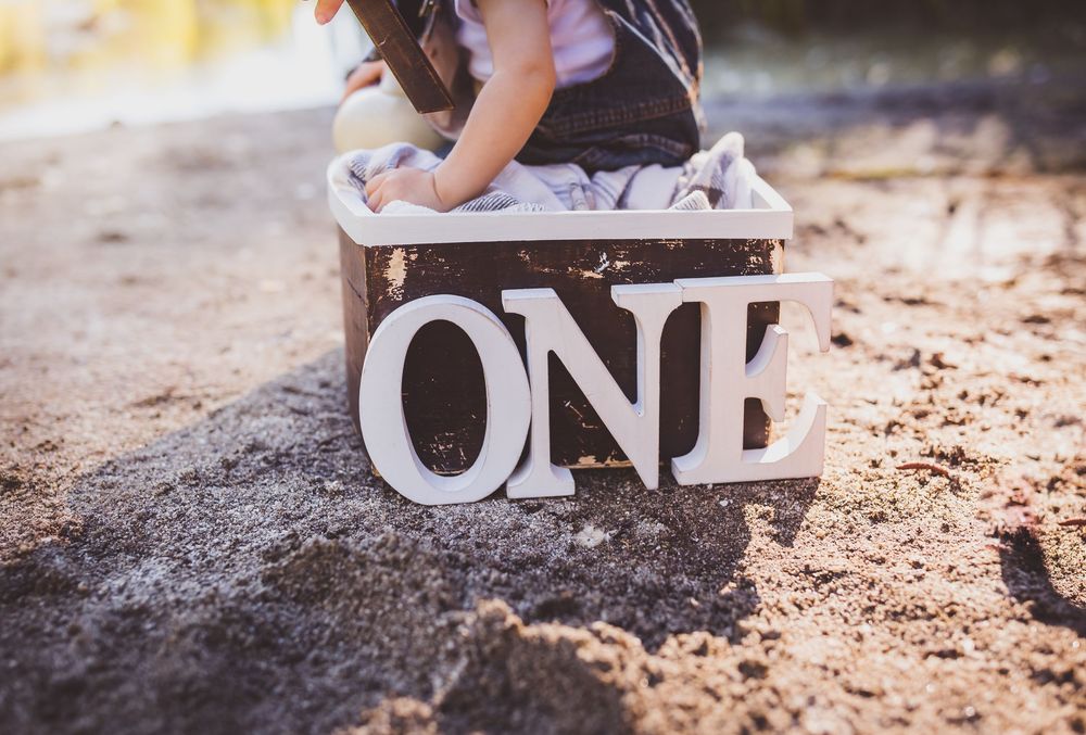 Wooden blocks spelling 'ONE' sit on a natural outdoor surface with blurred greenery in the background.