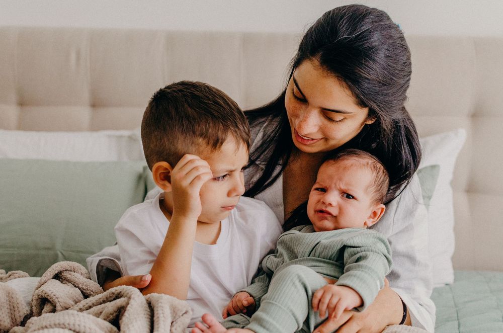 Family shares tender moments together while relaxing on light colored bedding.
