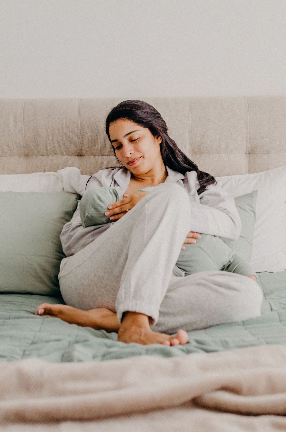 Person resting peacefully on bed wearing grey loungewear in natural light setting.