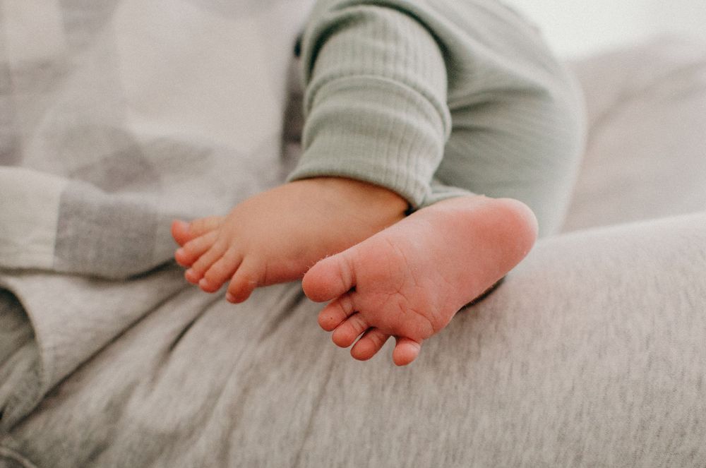 Close-up of tiny baby feet resting on soft grey bedding.