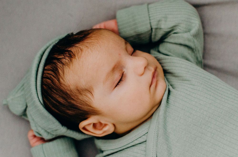Baby sleeping peacefully in soft mint green clothing on light colored bedding.