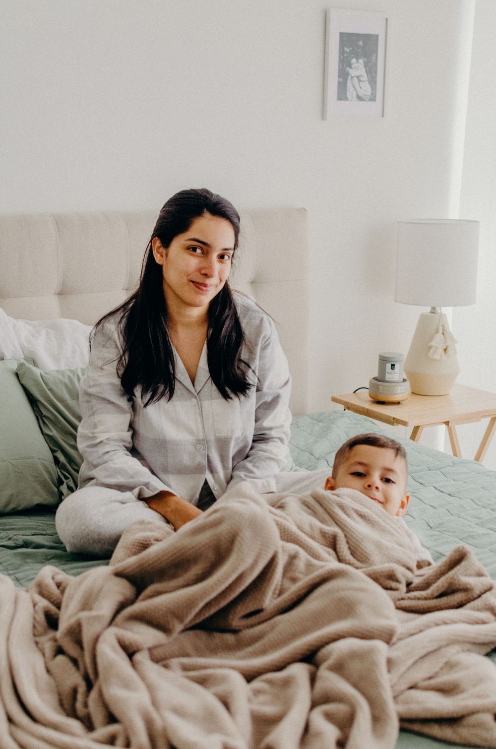 Family relaxing together on bed with cozy blanket in bright white bedroom.