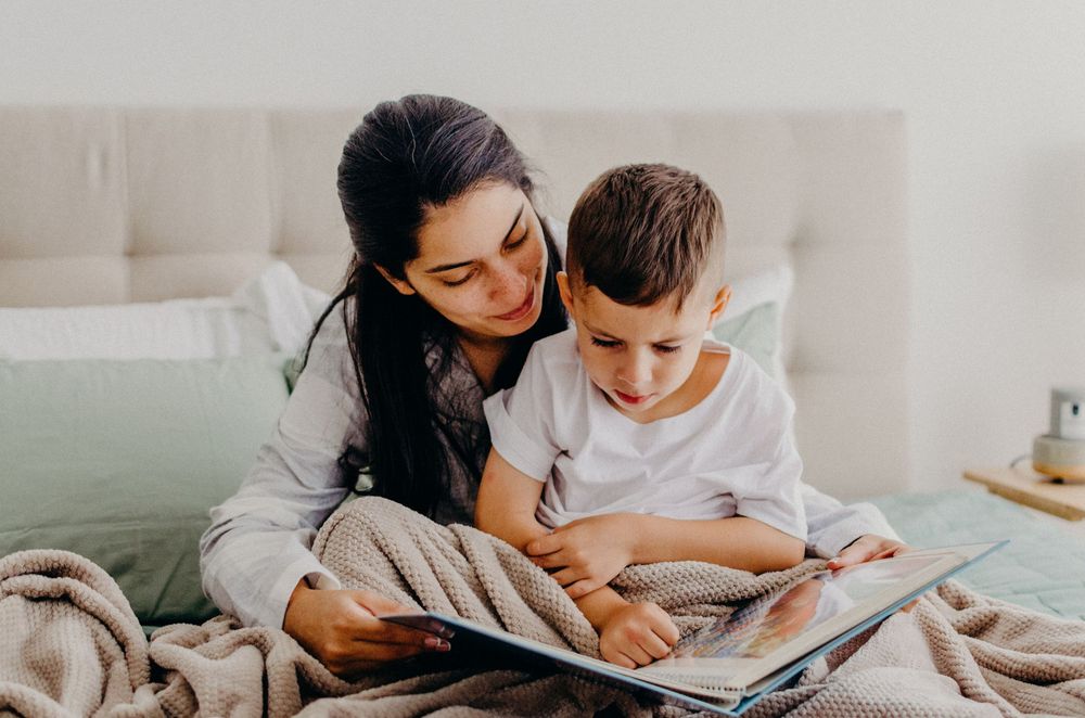 A parent and child share an intimate reading moment together on a couch.