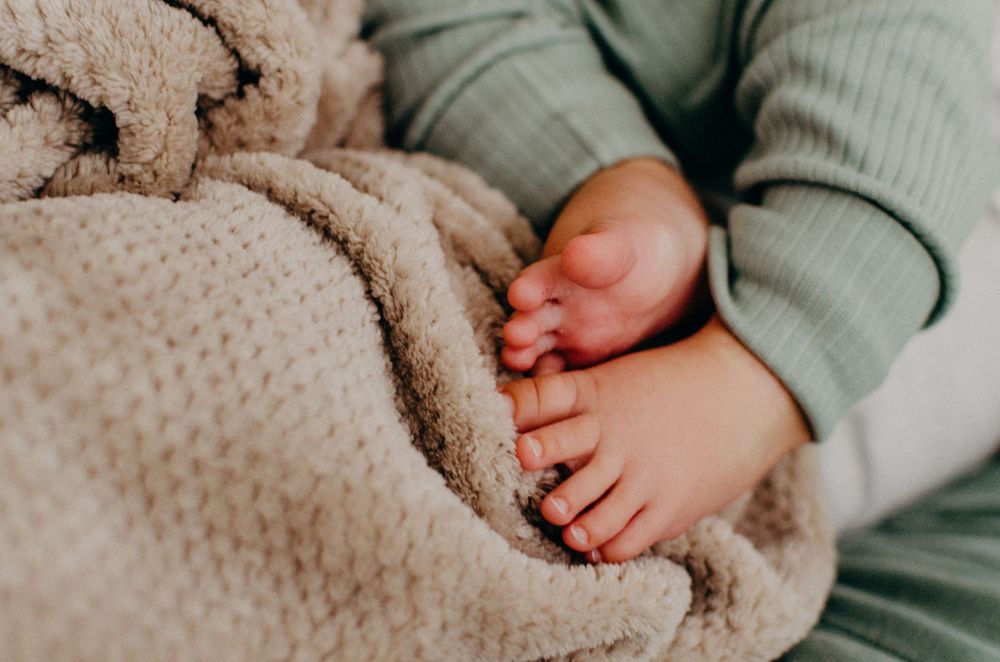 Baby's feet resting on plush beige knit blanket texture.