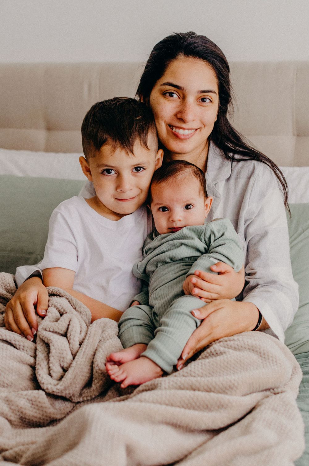 Family snuggling together on couch under beige blanket in intimate lifestyle photography series.