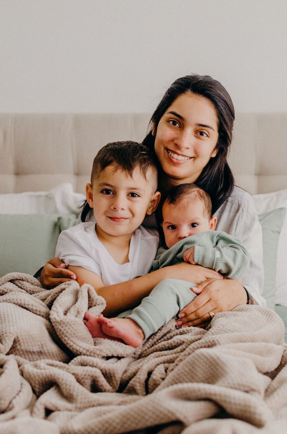 Family cuddles together on bed sharing tender moments with their new baby.