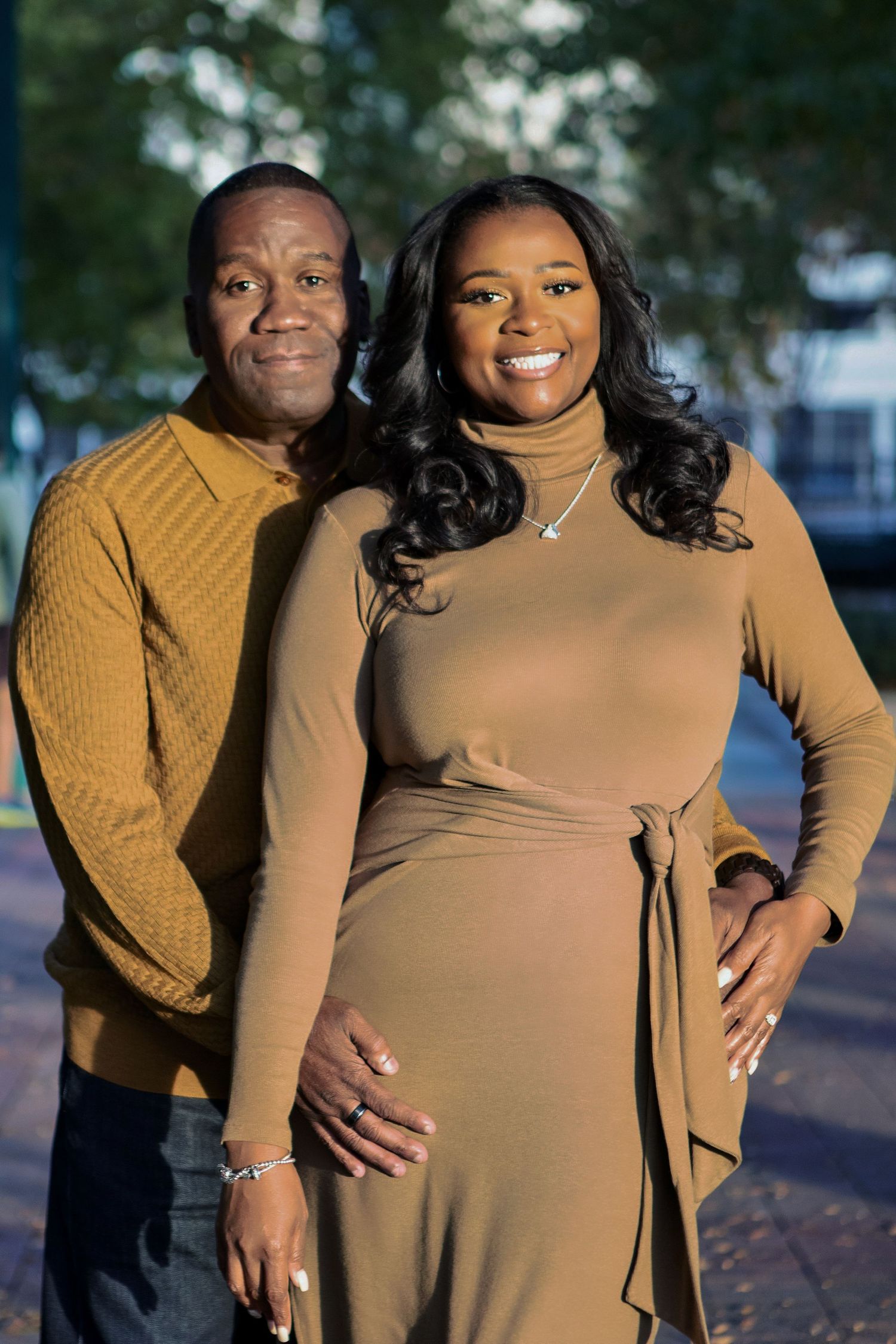 A couple wearing matching tan and brown outfits poses together outdoors for a series of casual engagement photos.
