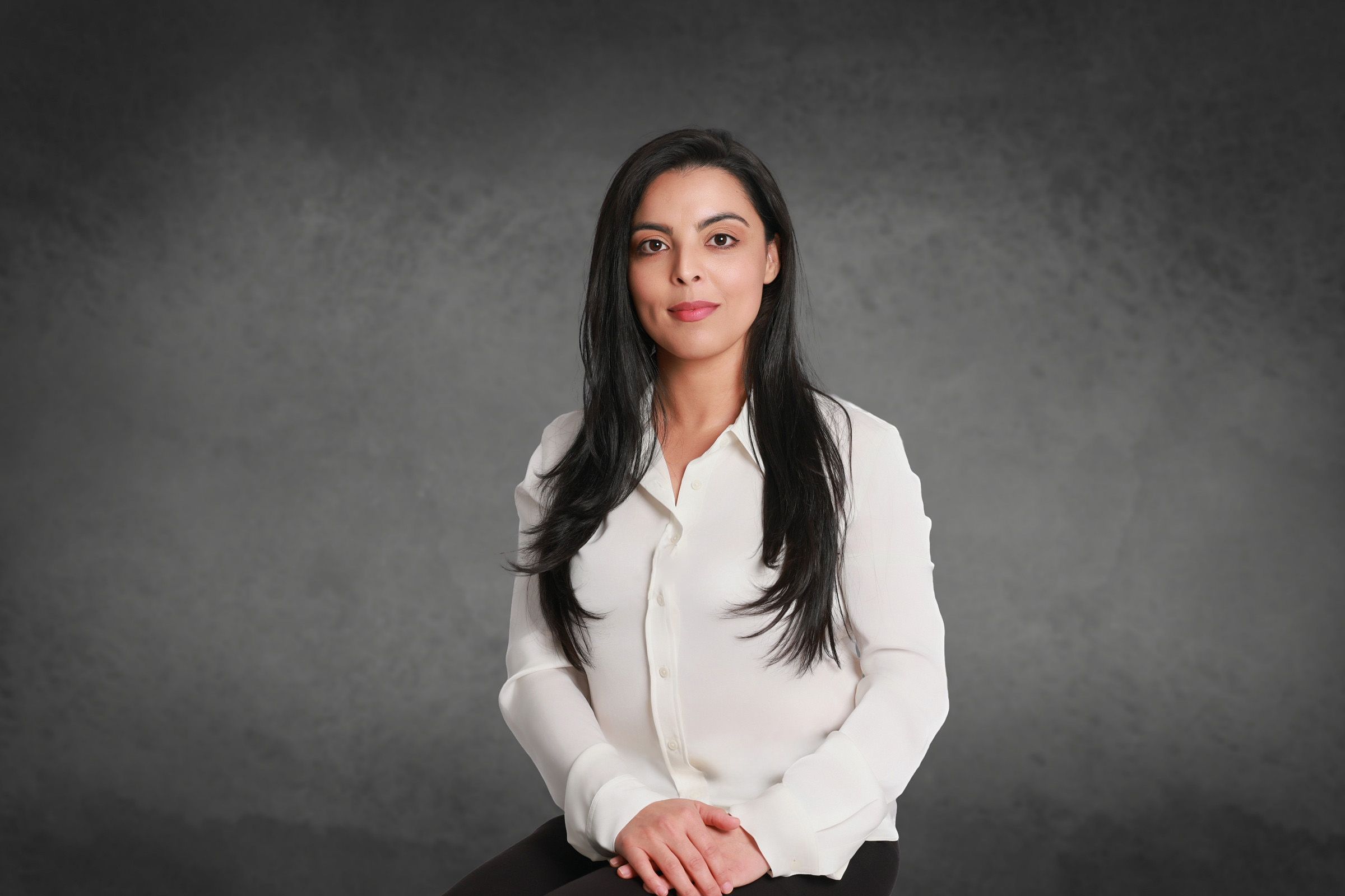 Professional portrait of a woman in a white button-down shirt against a dark gray background.