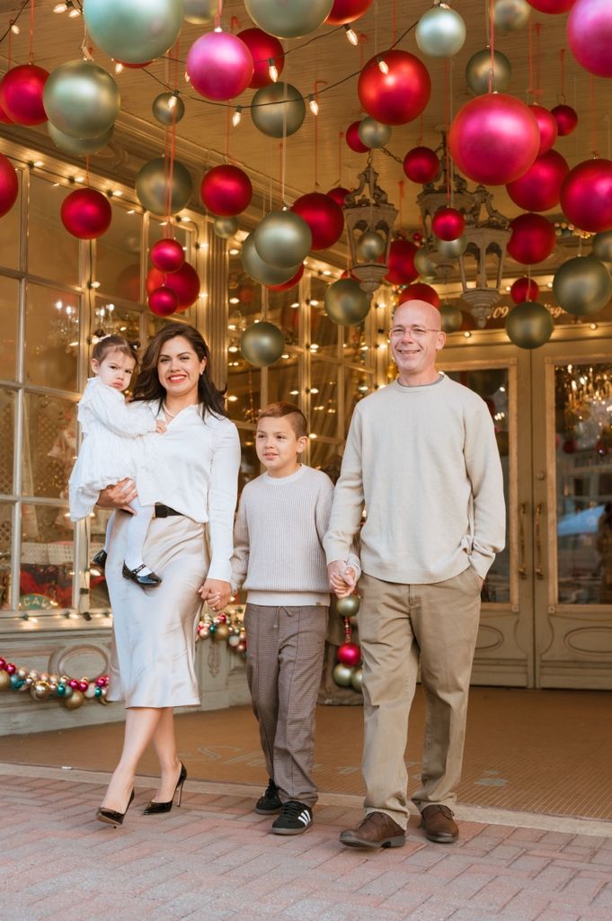 Family walking together under festive red and silver Christmas ornaments hanging from an indoor ceiling.