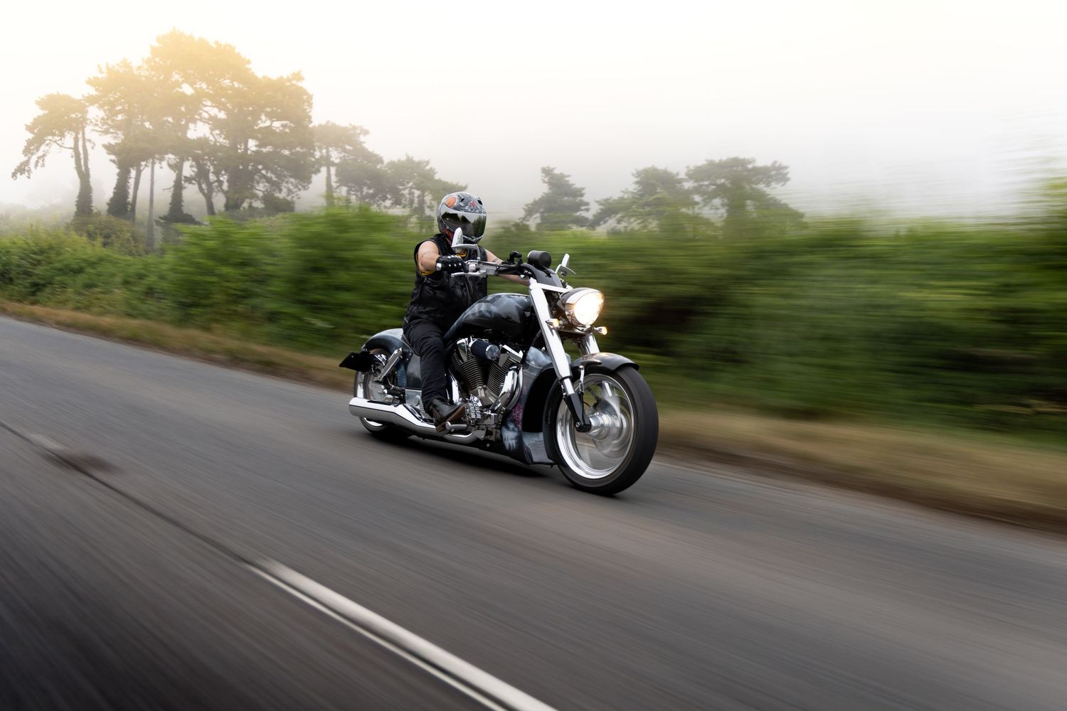 A motorcycle rider speeds down a winding road with motion blur creating a sense of dynamic movement.