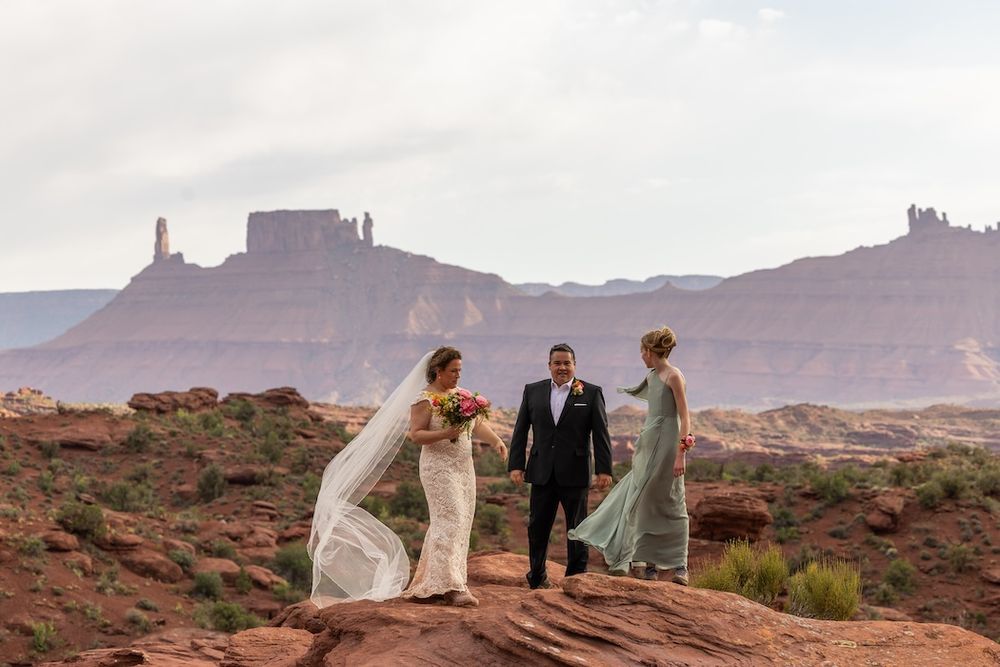 A wedding party poses against the stunning backdrop of Monument Valley's red rock formations and desert landscape.