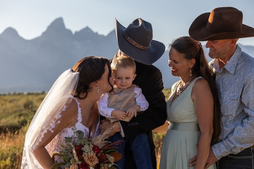 A romantic outdoor wedding ceremony takes place against a backdrop of majestic mountain peaks at sunset.