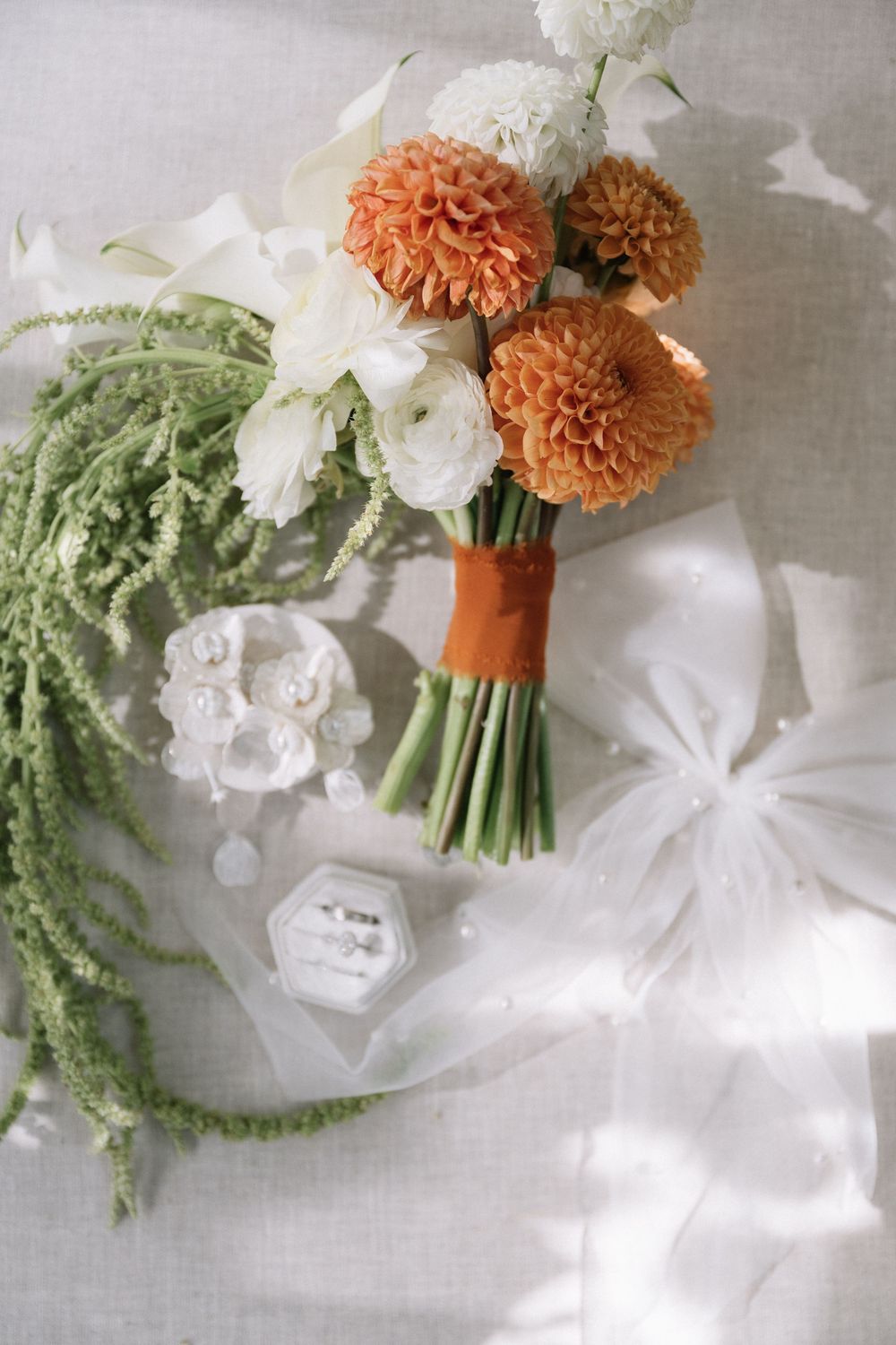 Wedding bouquets featuring orange dahlias and white flowers with cascading greenery on light linen background.