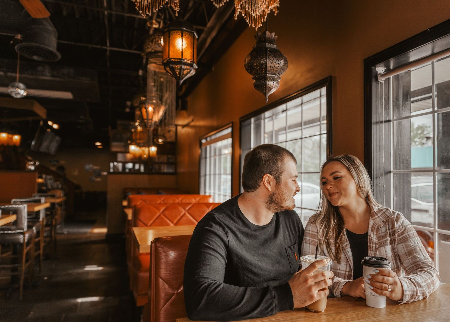 Couple sitting close together in a warmly lit cafe booth, sharing coffee and conversation.