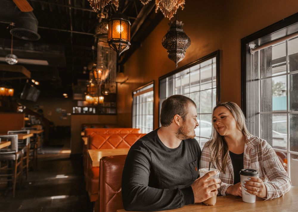 Couple sitting close together in a warmly lit cafe booth, sharing coffee and conversation.